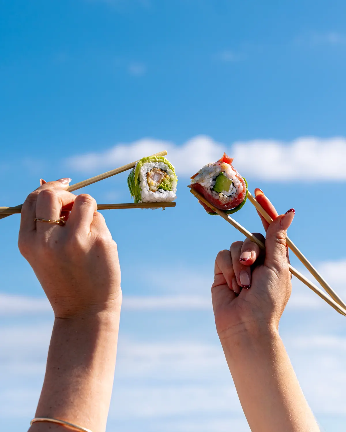 Deux rolls tenus aux baguettes devant le ciel bleu