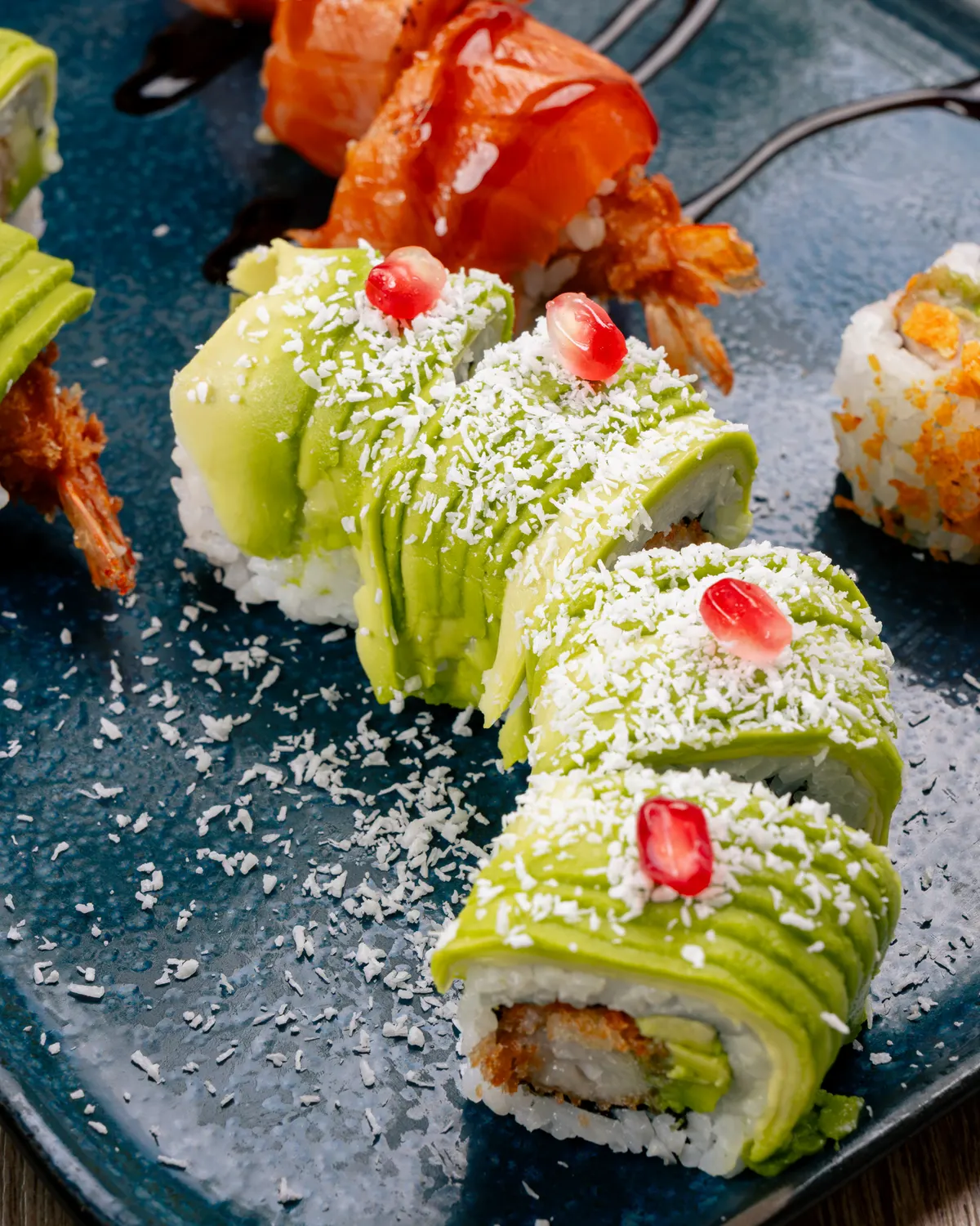 Rolls signature recouverts d’avocat, coco râpée et grain de grenade, sur assiette ardoise chez Mas Sushi