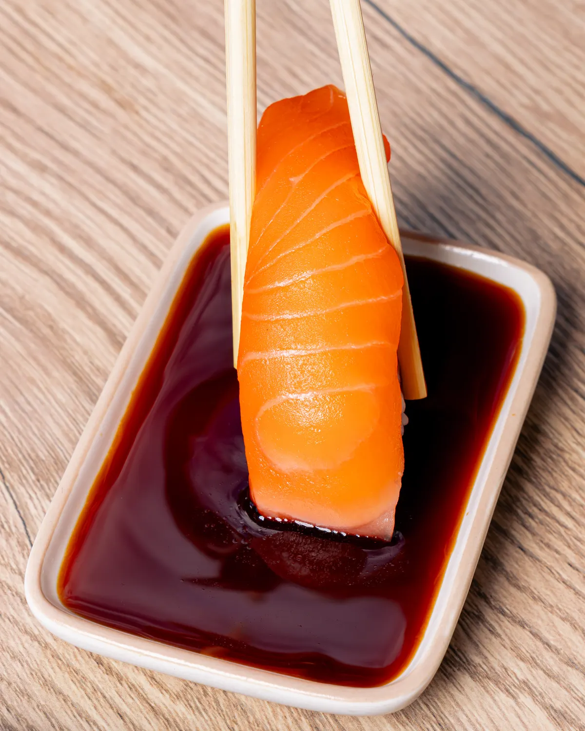 Un nigiri saumon trempé dans la sauce soja, tenu aux baguettes