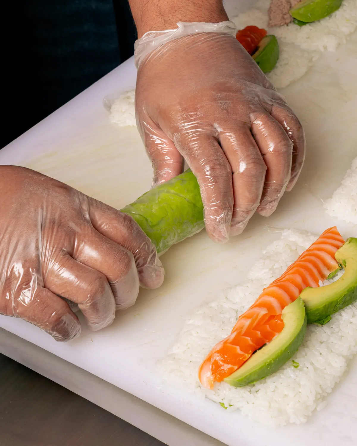 Un roll saumon avocat roulé à la main sur le plan de travail de Mas Sushi